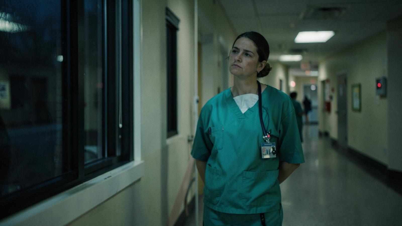 An emergency department nurse pausing by a corridor window during a night shift